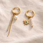 Two gold hoop earrings with decorative charms on a light fabric background