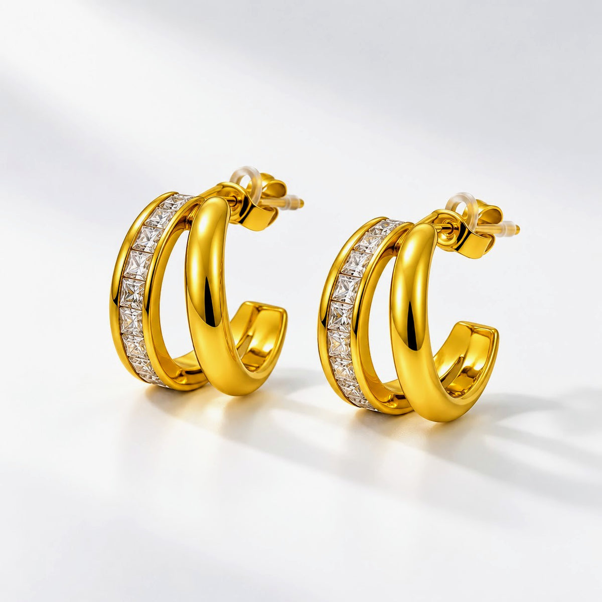 A pair of gold hoop earrings with a channel-set row of clear stones on the front, displayed on a clean white background.