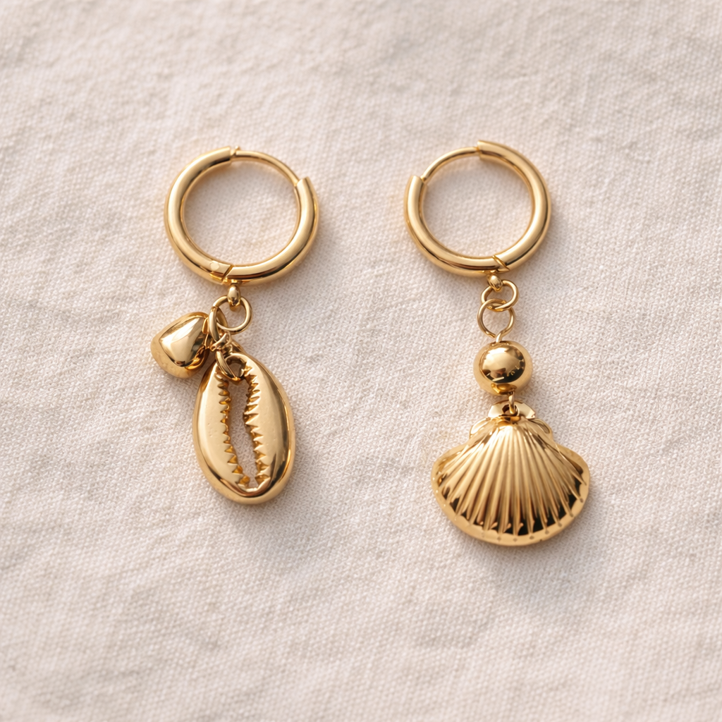 Gold hoop earrings with shell and cowrie shell charms on a light fabric background
