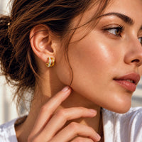 A close-up lifestyle shot of a woman wearing a small gold hoop earring with clear gemstones on her earlobe.