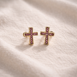 Pair of cross-shaped earrings with pink gemstones on a soft fabric background
