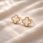 Gold and white butterfly-shaped earrings on a soft beige fabric background
