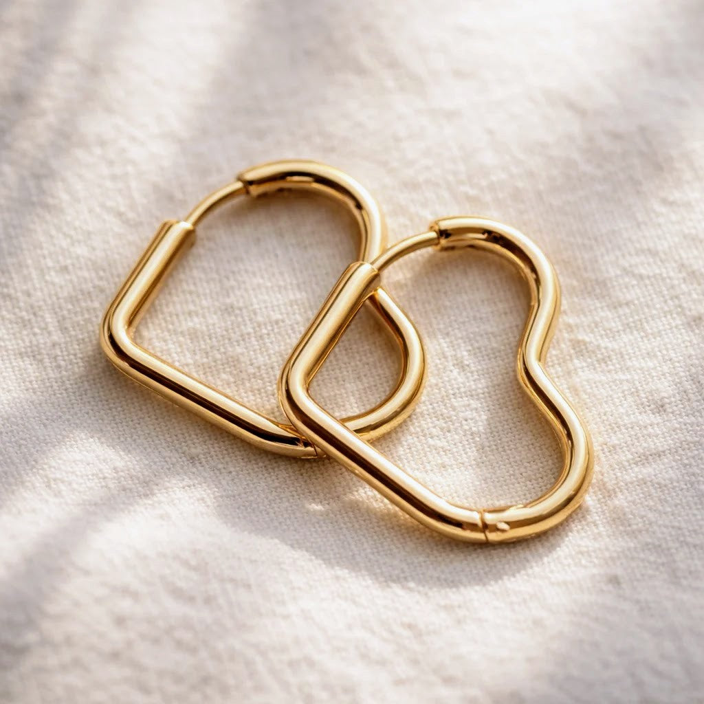 Two gold-toned metal heart-shaped hoop earrings resting on a textured off-white fabric background.