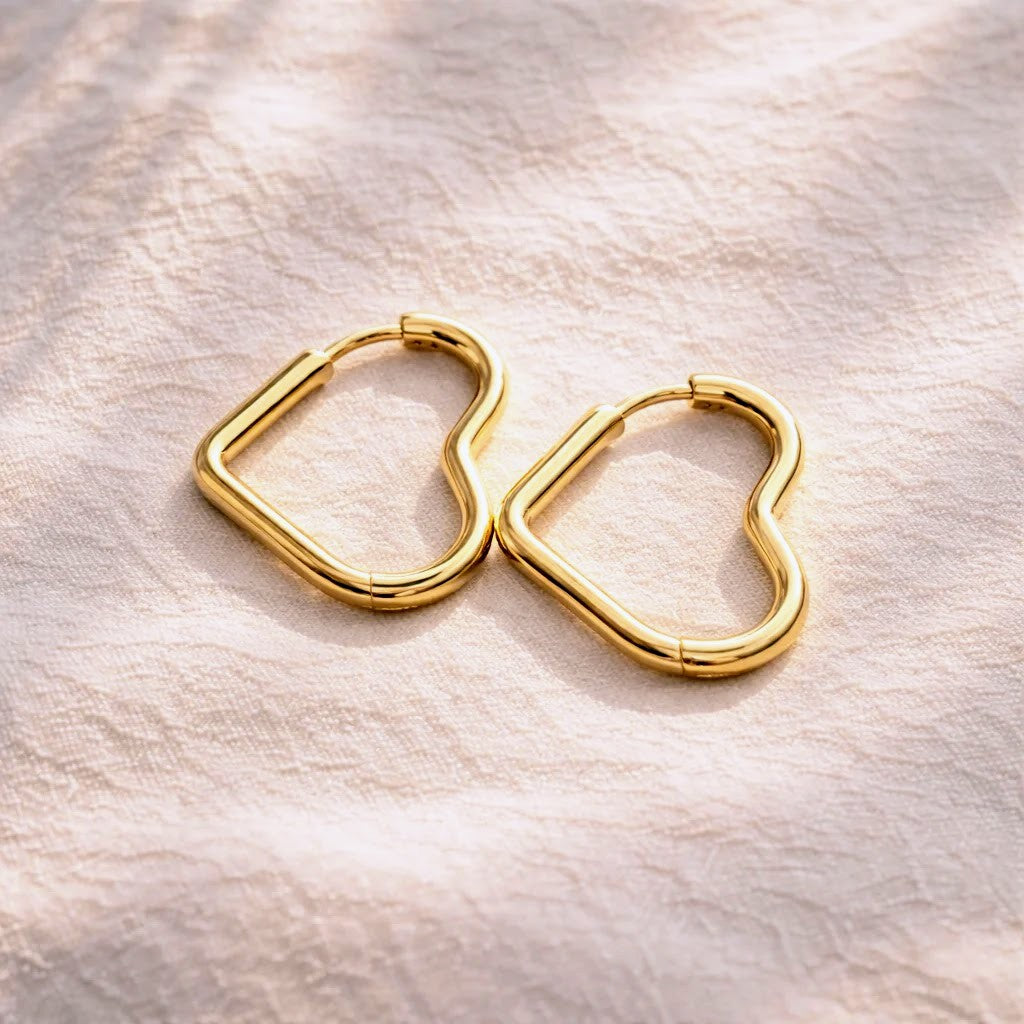 A pair of gold heart-shaped hoop earrings resting on a textured, light beige fabric background.