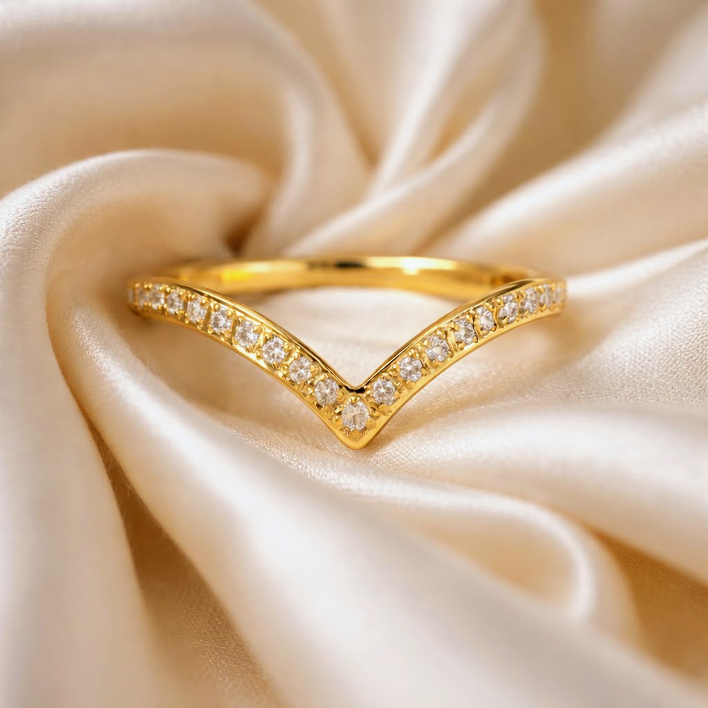 A gold V-shaped ring set with small clear stones, resting on draped cream satin fabric.