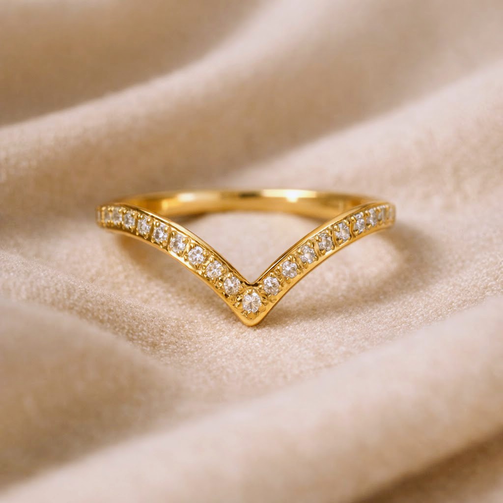 A gold V-shaped ring set with small clear stones, resting on a soft beige fabric background.