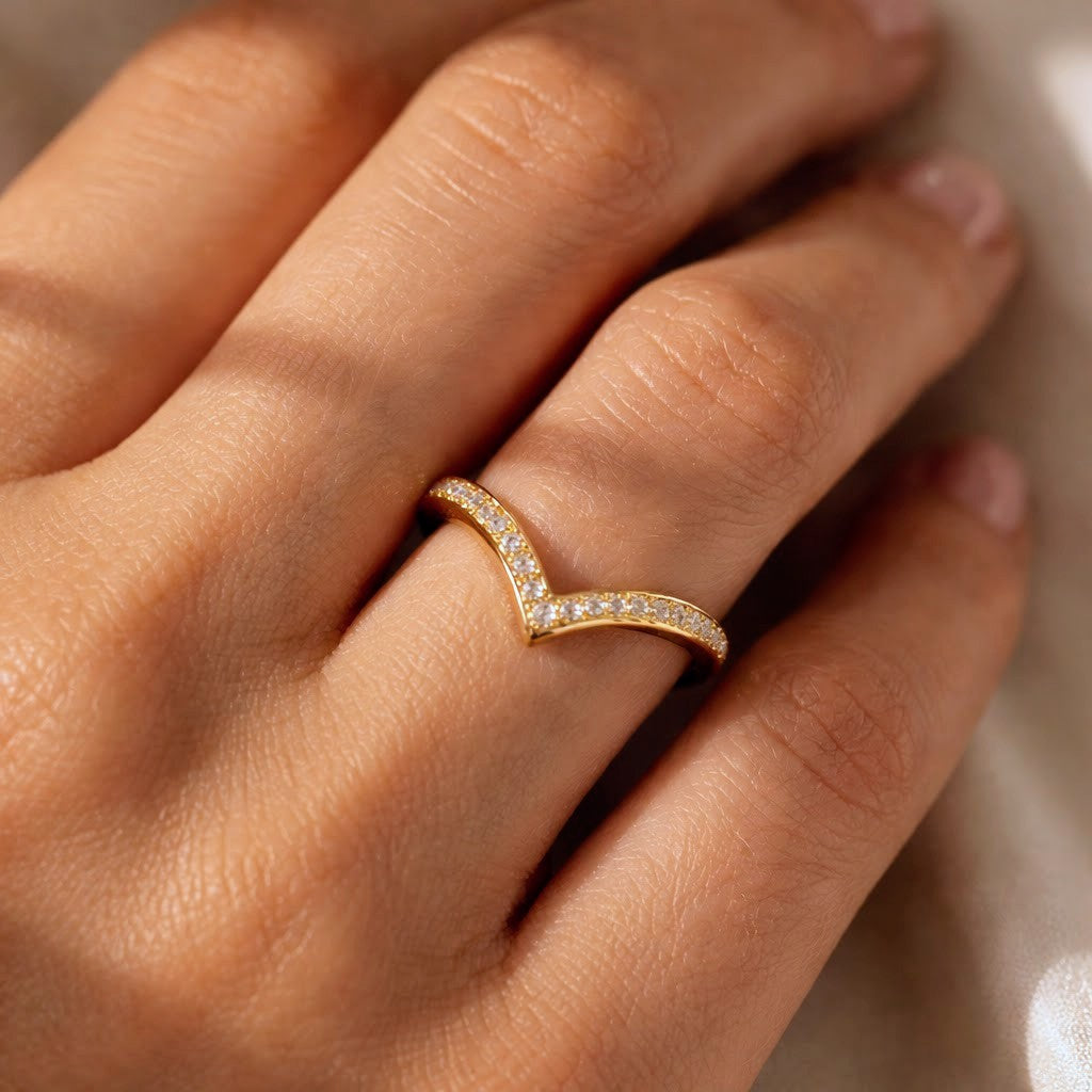 A close-up of a hand wearing a delicate gold ring with a V-shaped curve set with small clear stones.