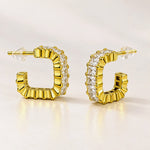 A pair of gold huggie hoop earrings with clear rectangular baguette-cut stones, shown on a clean white background.