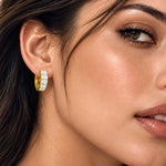 A close-up of a woman's ear wearing a small gold huggie hoop earring set with a row of clear stones.