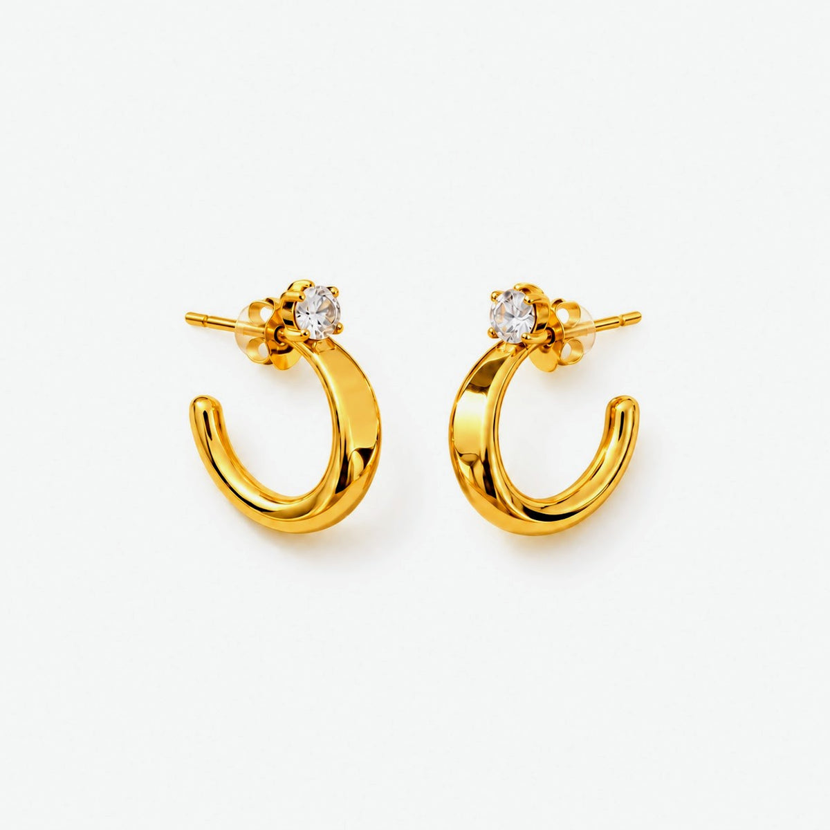 A pair of gold crescent-shaped hoop earrings with a small round clear gemstone at the top, displayed on a clean white background.