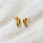 A pair of polished gold teardrop-shaped stud earrings resting on a textured, off-white fabric background.