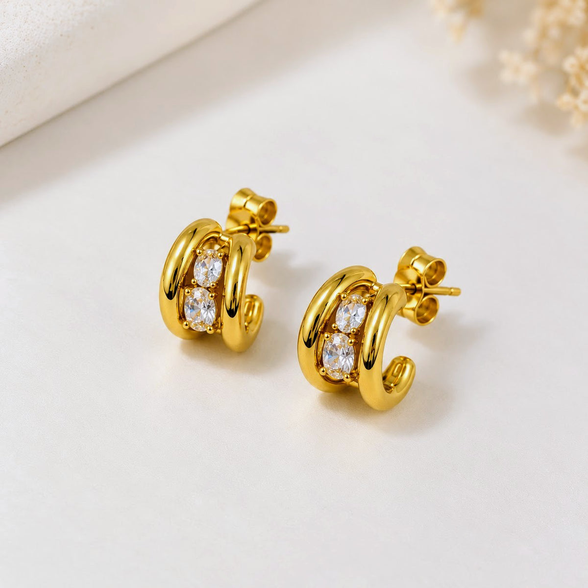 A pair of gold huggie hoop earrings with clear cubic zirconia stones, displayed on a clean white surface.