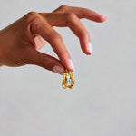 A close-up of a hand holding a small gold ring with three clear round-cut gemstones against a plain light gray background.