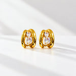 A pair of gold huggie hoop earrings with three clear oval gemstones on each earring, displayed on a clean white surface with soft diagonal shadows.