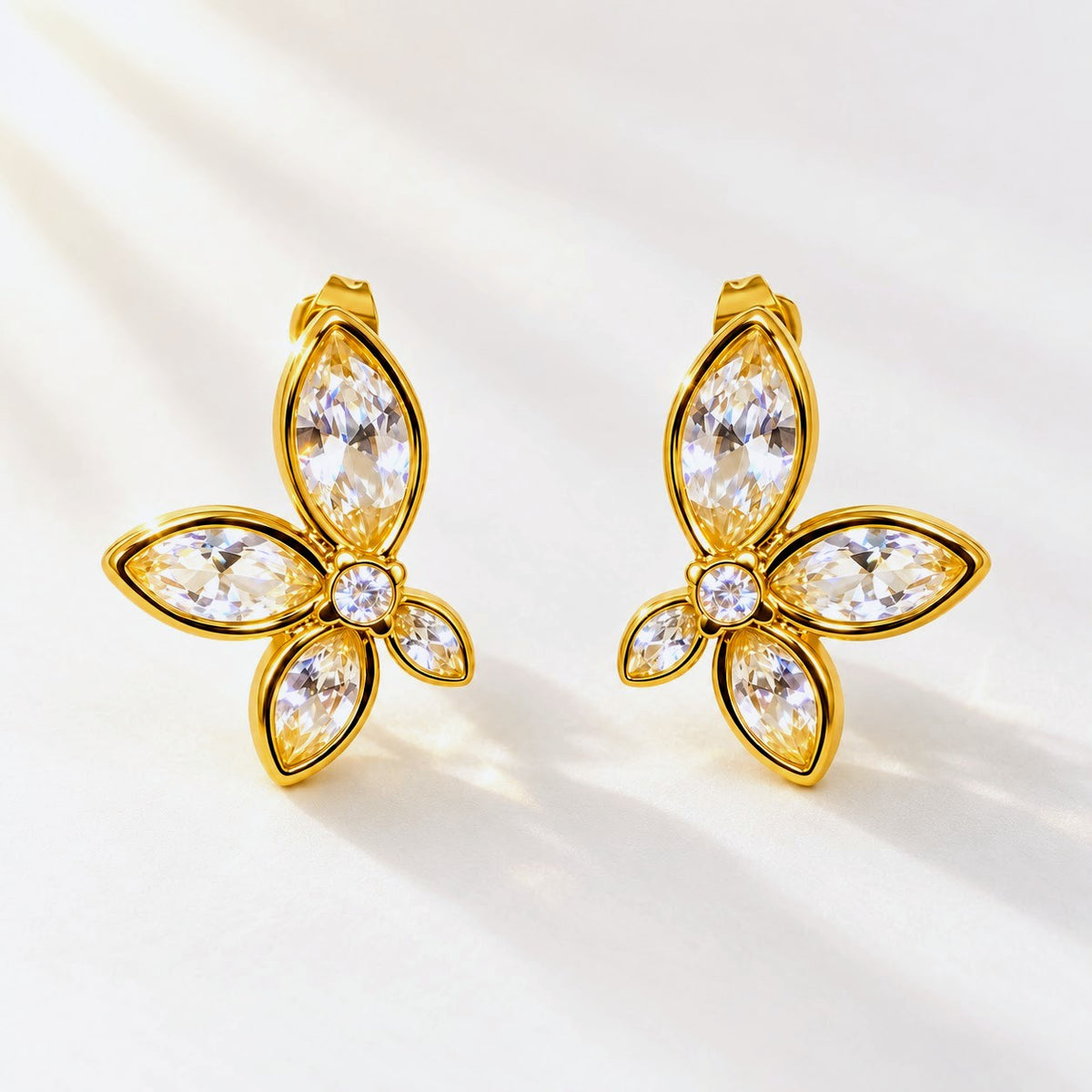 A pair of gold butterfly-shaped stud earrings with marquise-cut clear crystals, displayed on a clean white background with soft shadows.