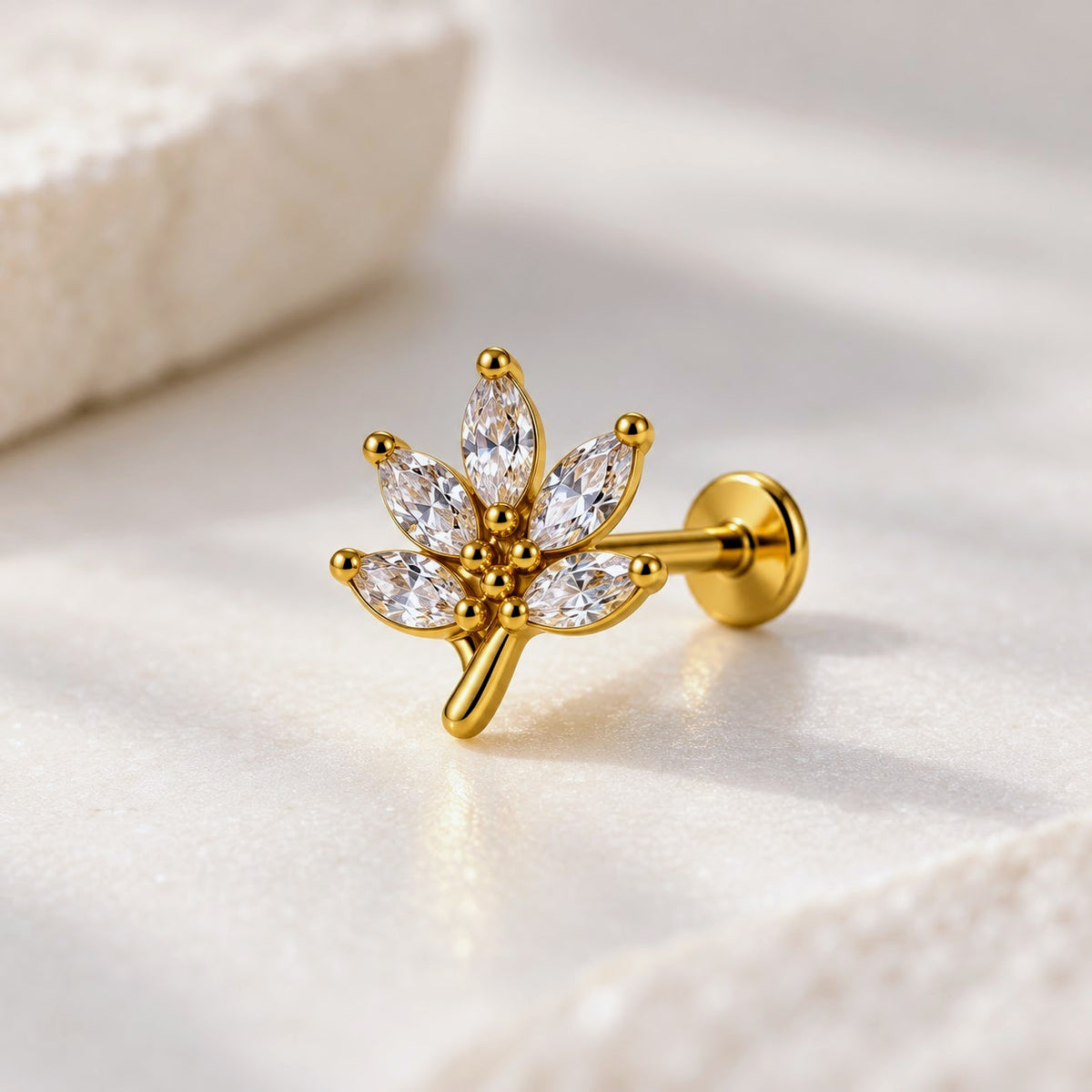 A gold leaf-shaped stud earring with marquise-cut clear crystals, displayed on a soft white textured surface.