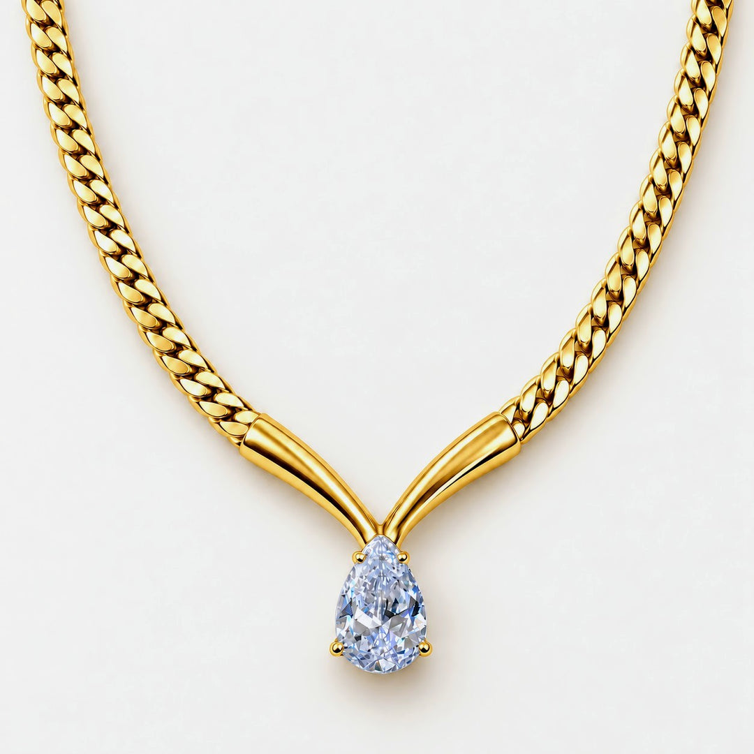 A close-up of a gold chain necklace with a Y-shaped connector and a pear-cut light blue gemstone pendant, shown on a plain light background.