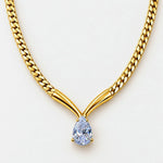 A close-up of a gold chain necklace with a Y-shaped connector and a pear-cut light blue gemstone pendant, shown on a plain light background.