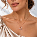 A close-up of a woman wearing a delicate rose gold necklace with a circular pendant featuring a swan design, styled with a champagne satin top.