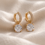 Gold hoop earrings with round gemstones on a beige fabric background