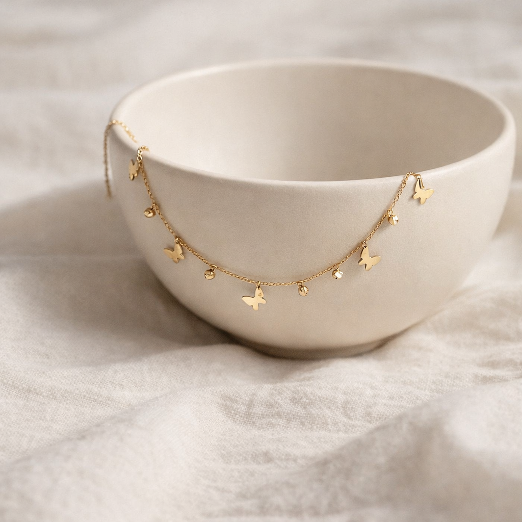 Gold necklace with butterfly pendants draped over a white bowl on a light fabric background